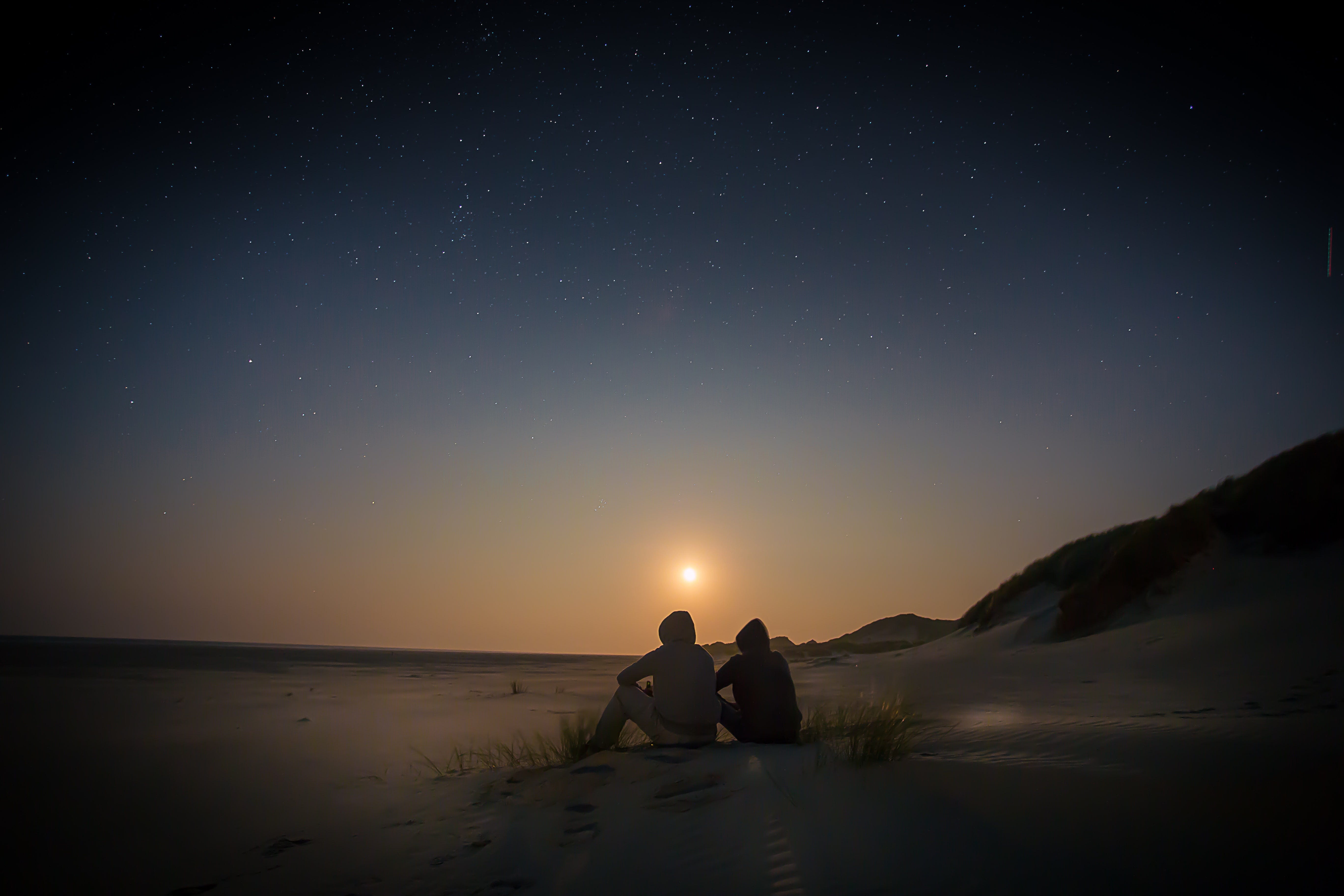 Two people sitting by the beach, either at dawn or sunset.