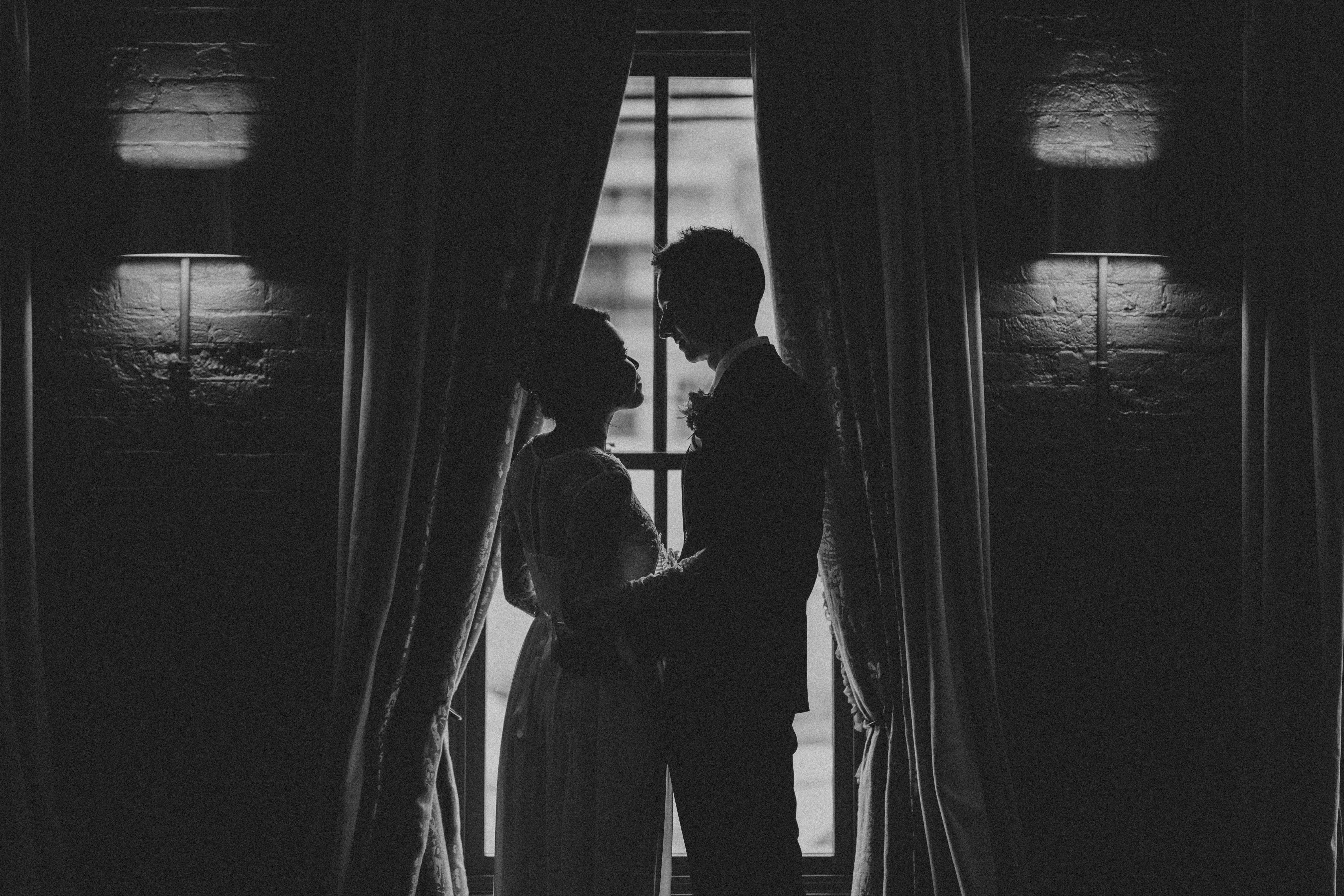 a bride and groom stand facing each other in front of a window
