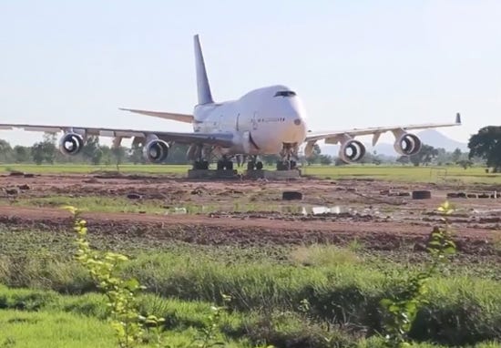 A photograph of a somewhat run down Boeing 747 parked in an open field.