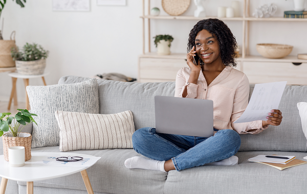 Image of woman on phone while reviewing work on laptop.