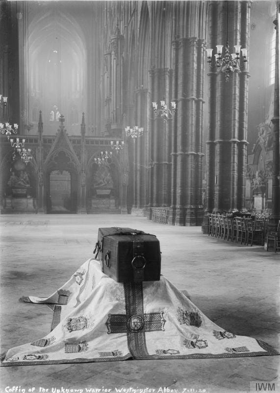 A black and whiteb image of the coffin containing the remains of an unknwon British soldier of the Great War. The coffin rests on a standard draped over a low platform and lies alone in the vaulting hall Westminster Abbey. The photo has a hazy, dreamy quality to it.