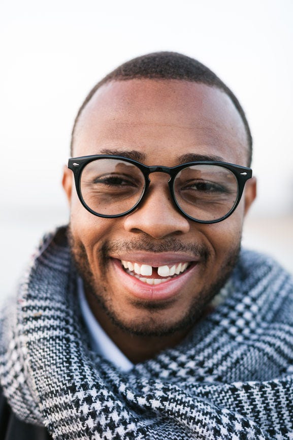 A young black man with glasses and a scarf, smiling