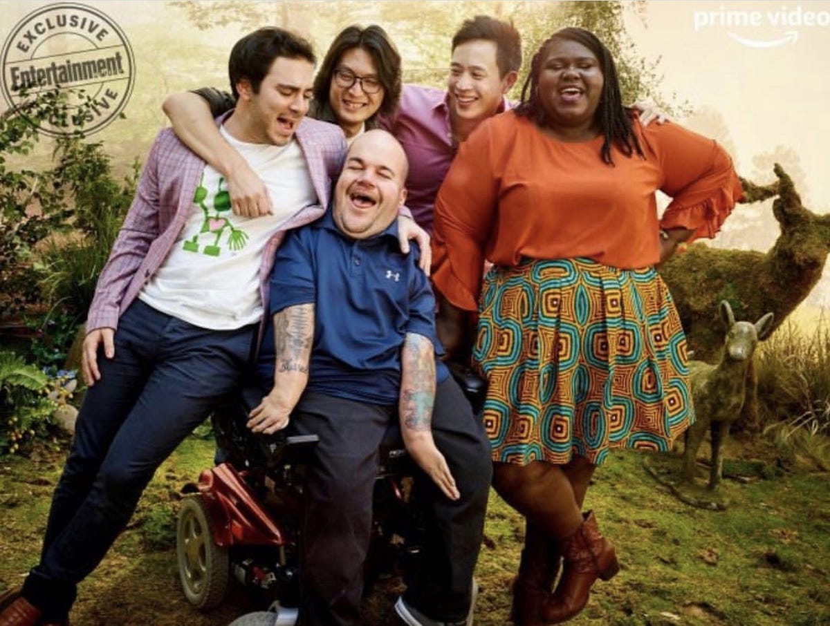 Asta Philpot, in his motorized wheelchair, sits surrounded by the cast of "Come As You Are," including (from left to right): Grant Rosenmeyer, director Richard Wong, Hayden Szeto, and Gabourey Sidibe. All subjects are smiling widely and laughing. 