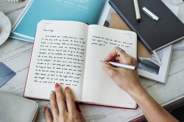 Woman holding pen writing on lined pages of a journal.