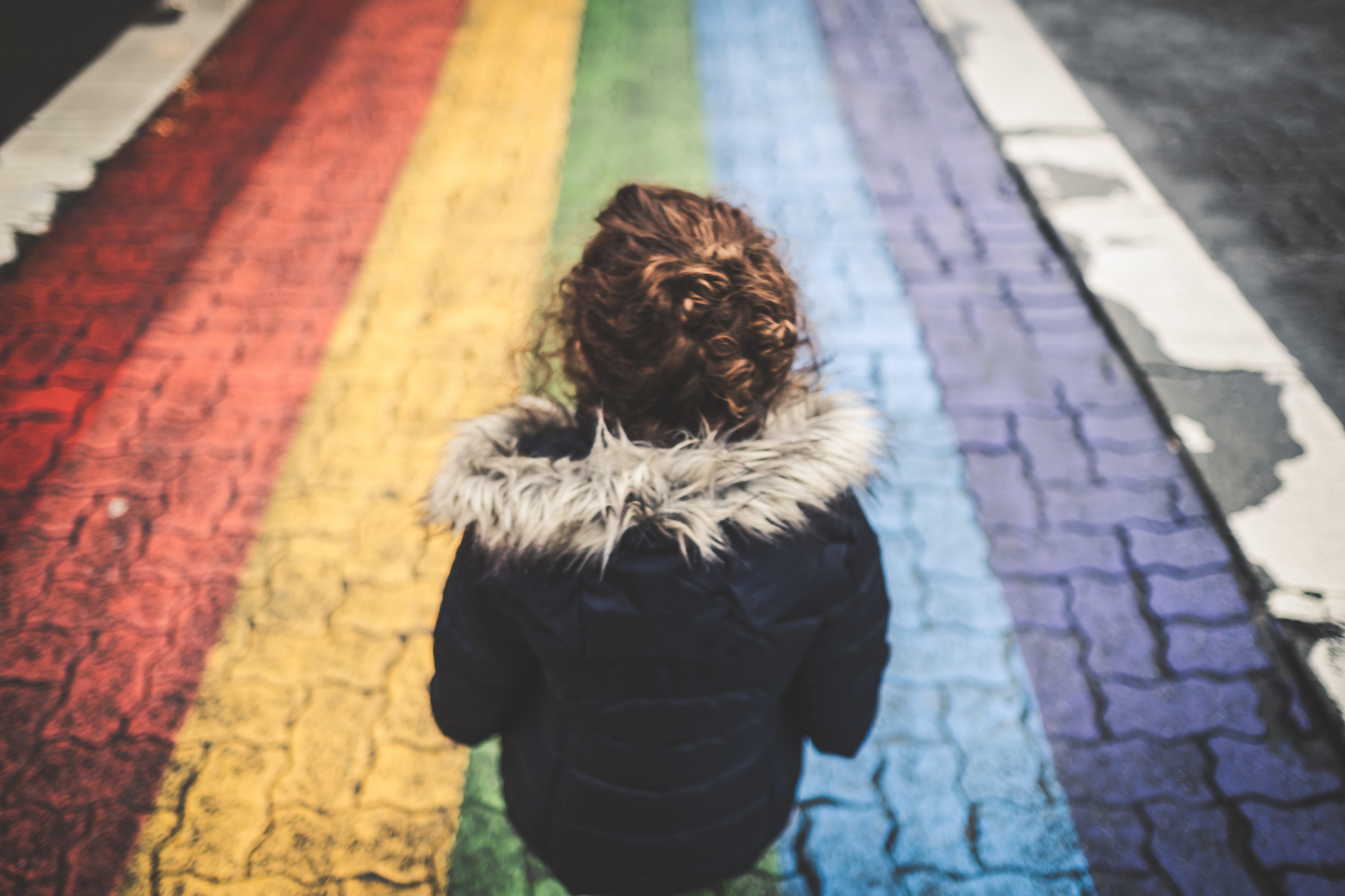 Kid seen from the back, walks on a rainbow-painted crosswalk