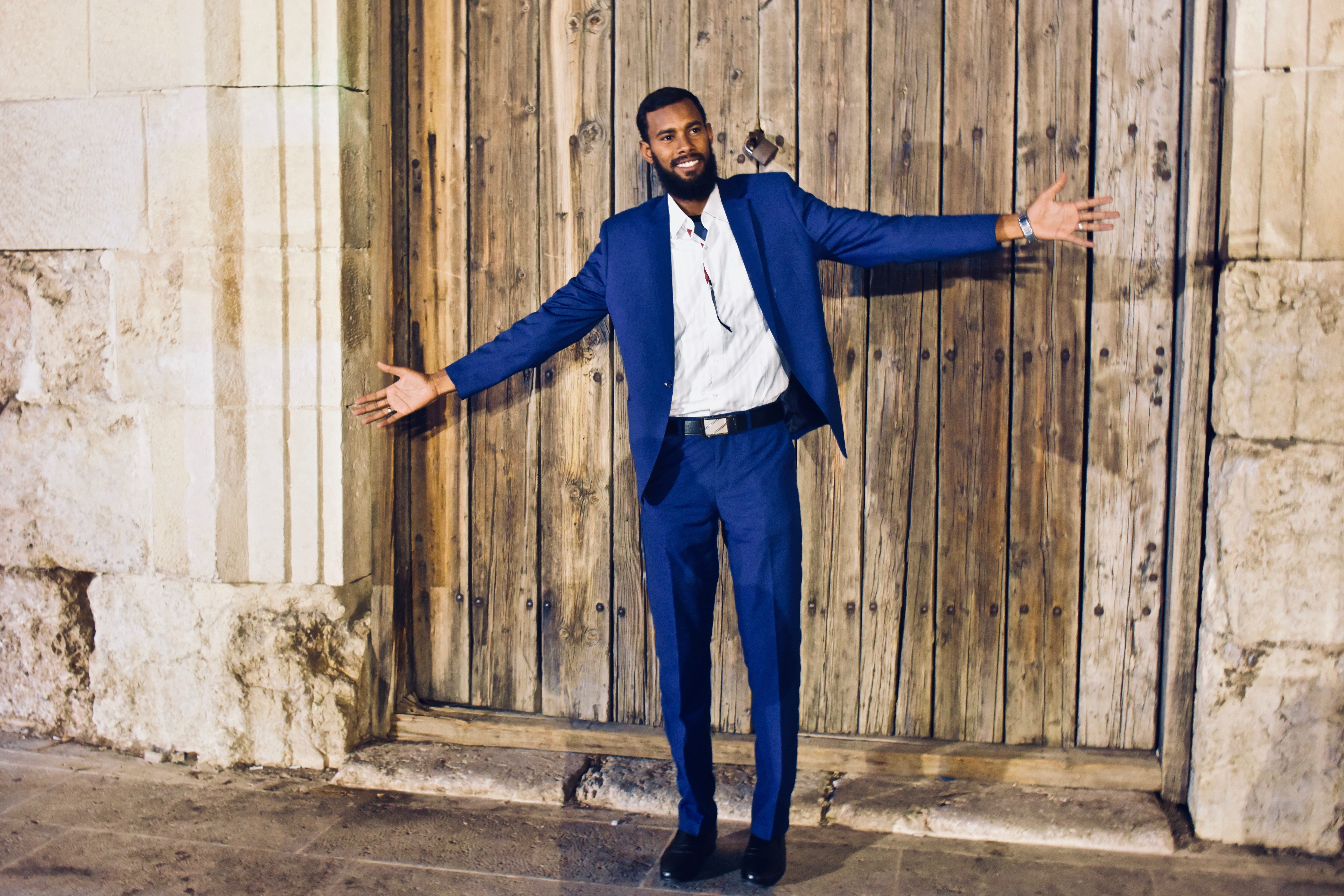 A tall man in suits standing in front of Ancient wooden gate