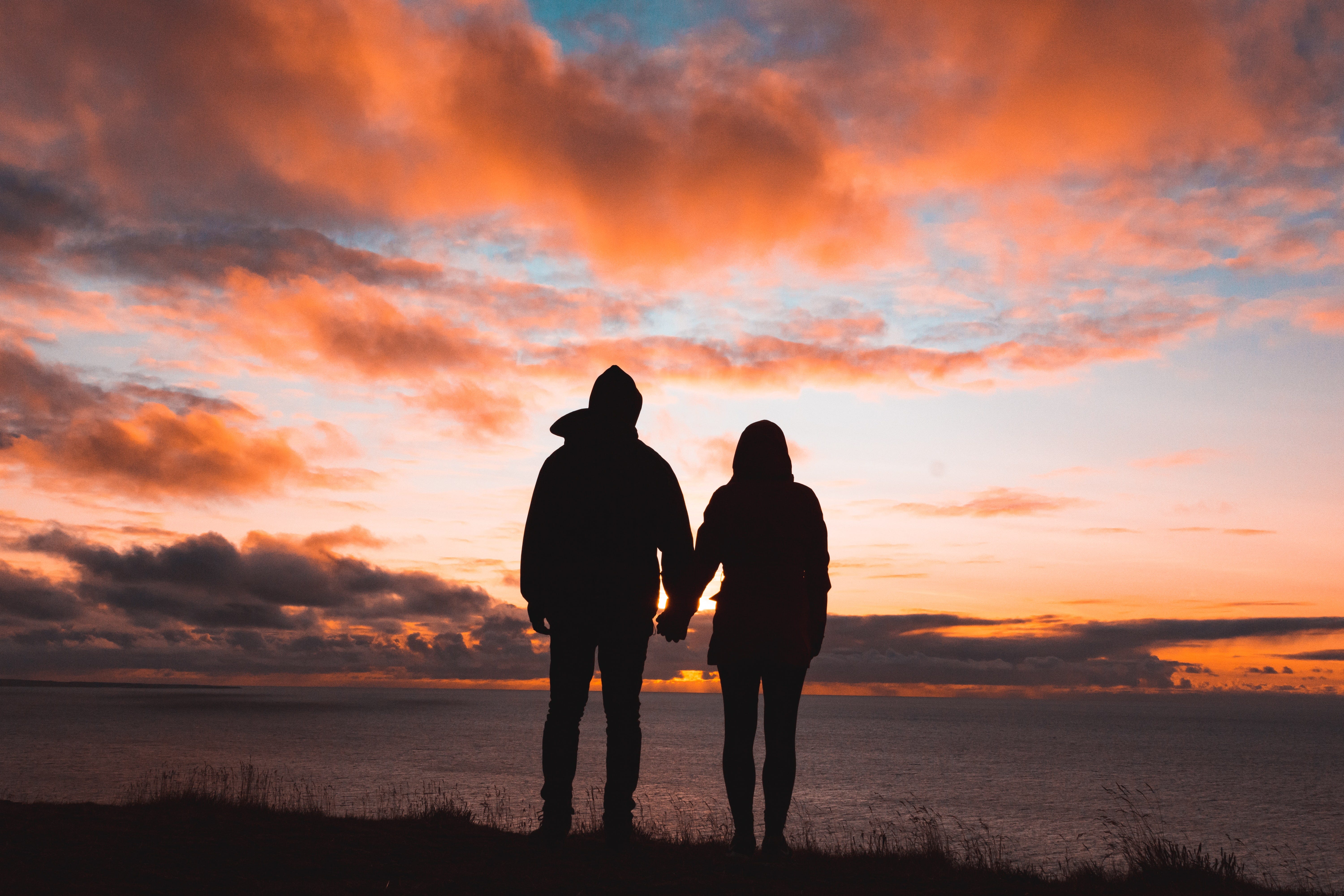 Couple standing on hill looking out over the sea and watching a sunset