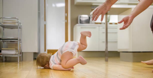 Baby falling face down onto the floor while parent’s hands are reaching towards them.