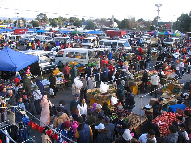 A busy market with lots of people, tents and vans
