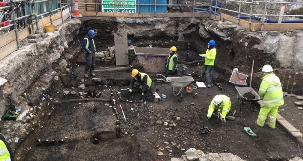 A photograph of an archaeological dig in Lapa do Picareiro. There are a group of archaeologists wearing yellow hi-viz vests and hard hats.