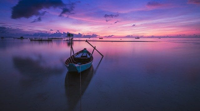 Purple hued sunset with rowboat. Image by Quang Le from Pixabay.