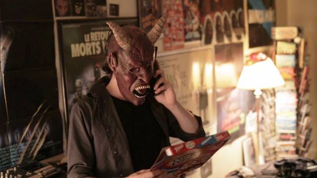 A man in a monster mask is on the phone while holding a pizza box.