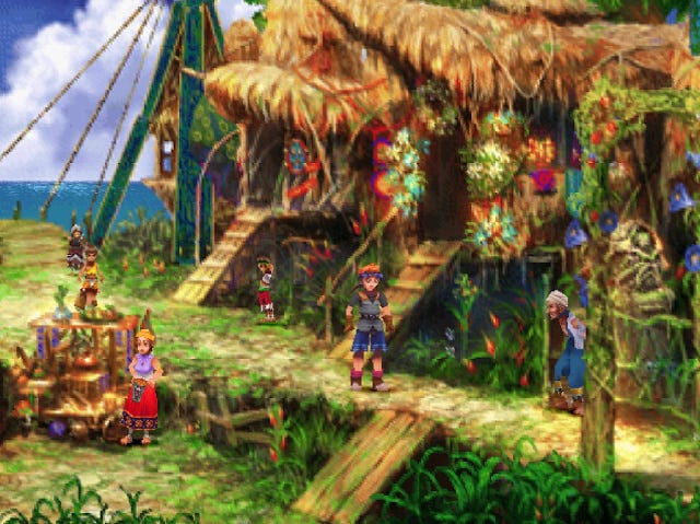 A screenshot from the game showing Serge, the main player character, standing outside of an island house in one of the colorful town areas of the game, with other folks nearby tending to their own various activities, and the sea in the distance toward the horizon.