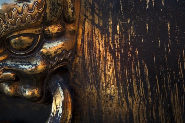 A golden door knocker in the mouth of a creature with a crown