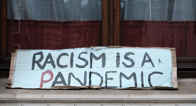 a wooden bench with the words racism is a pandemic painted in white, black and red.