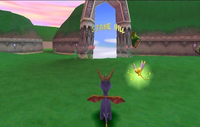 A screenshot from the game showing Spyro traversing a grassy plains area, heading toward an archway with the words “Stone Hill” floating inside, which will take the player to that area of the game.