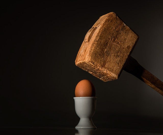 A wooden mallet is coming down atop an egg in a cup.