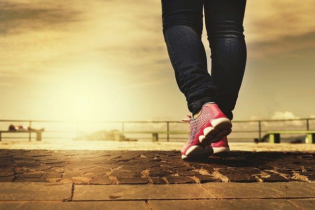 Person’s legs in motion walking in sneakers on a walking path near beach.