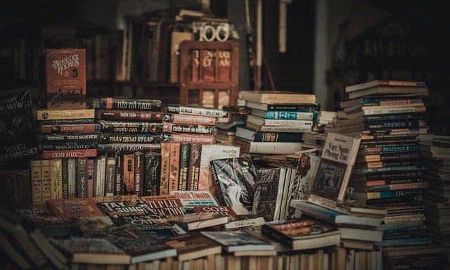 Books in piles with spines sitting vertically and horizontally, and with spines facing in towards the piles.