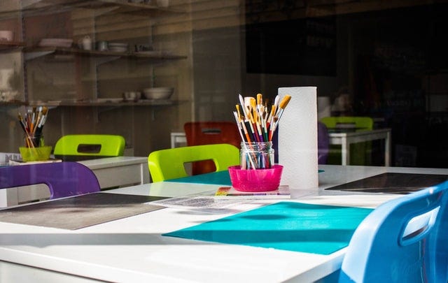 Paintbrushes and paper on a classroom table. Photograph courtesy of Charisse Kenion on Unsplash.