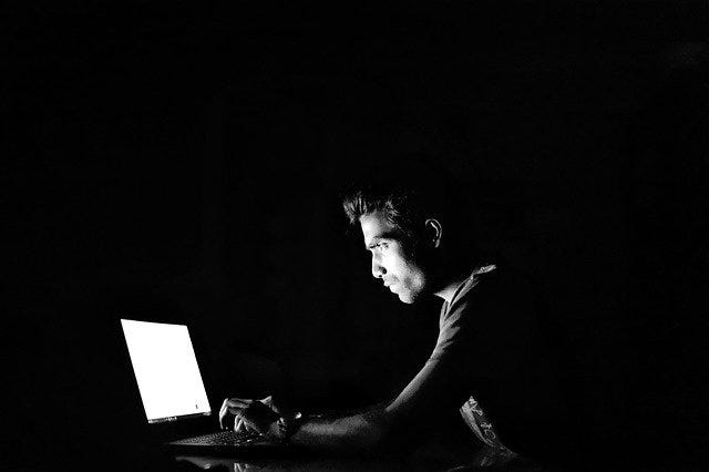 Man working on laptop in dark room (black and white photograph)
