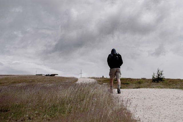 Person in black jacket and beige shorts walking under a grey sky