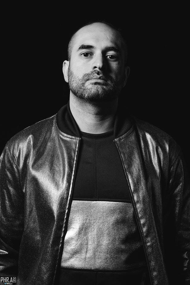 Black and white photograph of David Ordonez DJ, producer and new NFT Art Gallery founder and creator. David has a bald head, stubble and is wearing a black leather jacket.