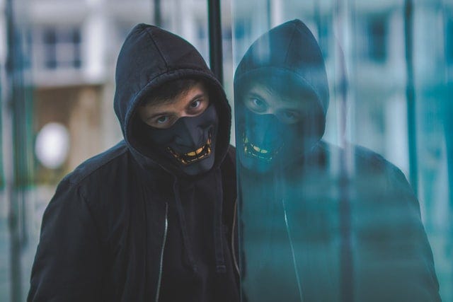 a person with a mask staring into a window with their reflection looking back at them.