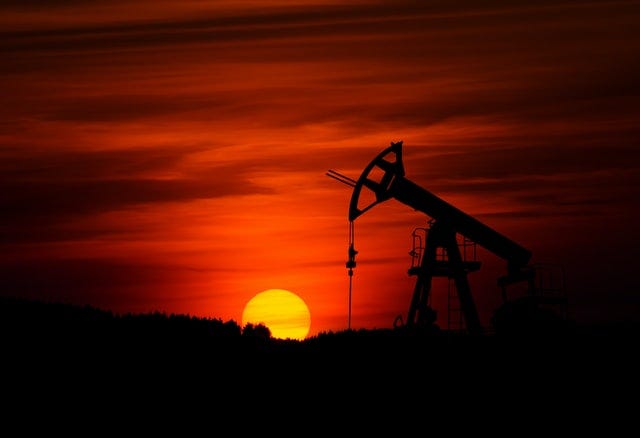 Silhouette of a pump-jack mining crude oil with a bright orange sunset in the background.