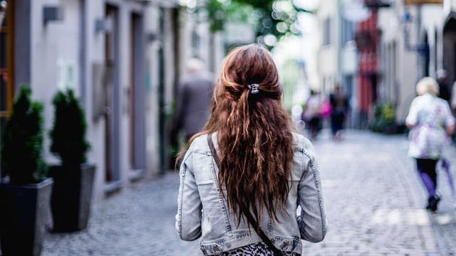 A person with long hair walking down a cobblestone street.