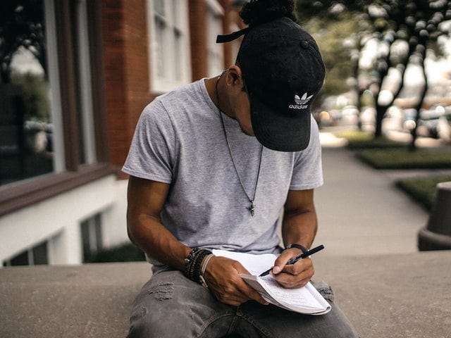 A student in a baseball cap makes notes in an exercise book