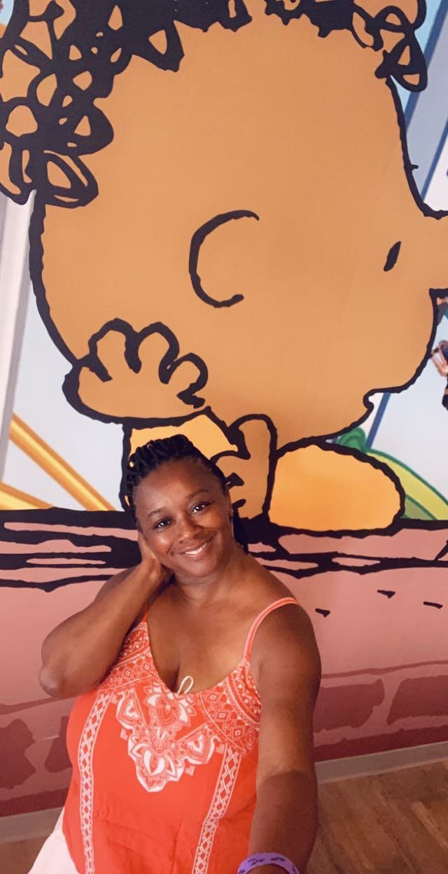 lady smiling hand on check standing in front of peanuts character Franklin