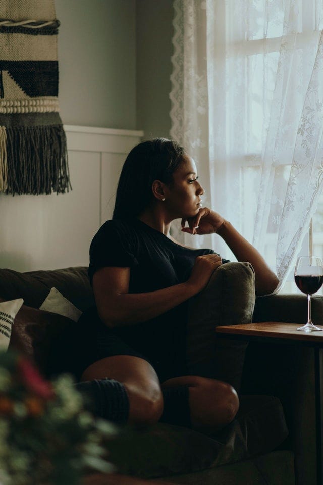 Woman looking out window with glass or red wine
