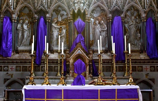 Statues above and altar and a crucifix on an altar shrouded in purple cloth, a Palm Sunday tradition in many churches.