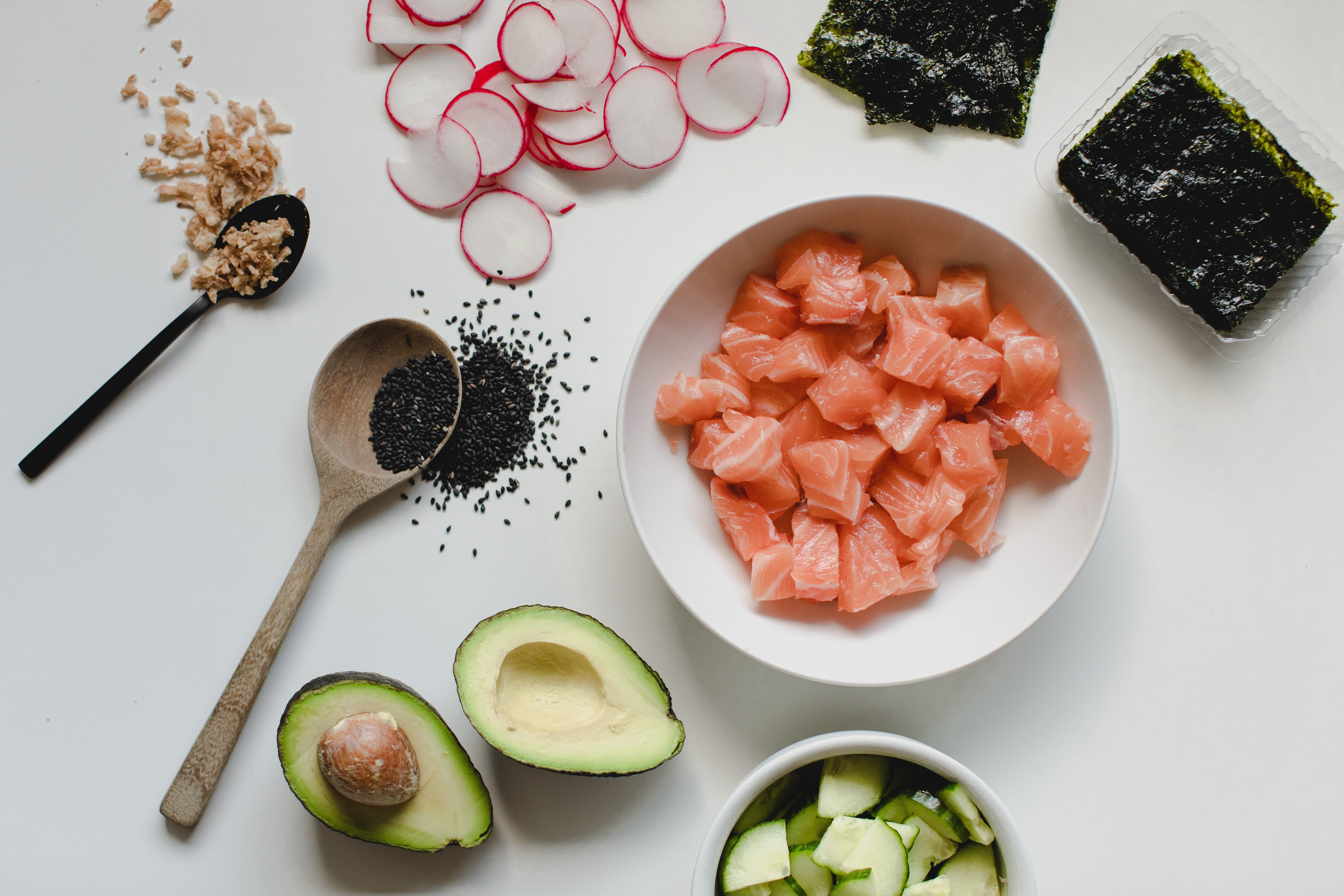 Salmon, avocados, cucumbers, and radishes on a table.