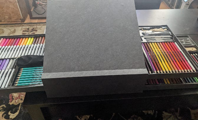 An art supplies set featuring markers and pencils on the left pull-out, colored pencils on the top pull-out on the right, and more colored pencils on the bottom pull-out on the right. The center is propped up to function as an easel.