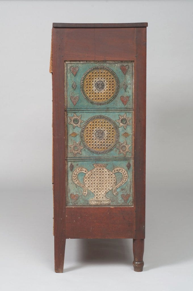 Side view of a wooden pie safe featuring a panel of colorfully decorated punched tin.