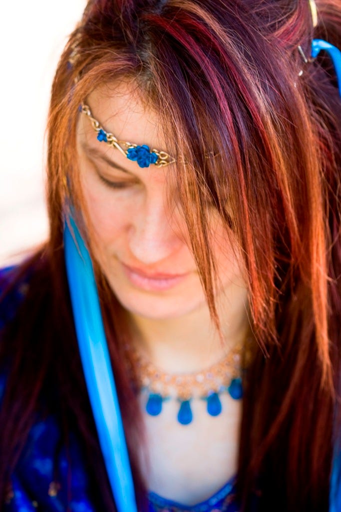 Young red-haired woman dressed in blue, looking down in contemplation.
