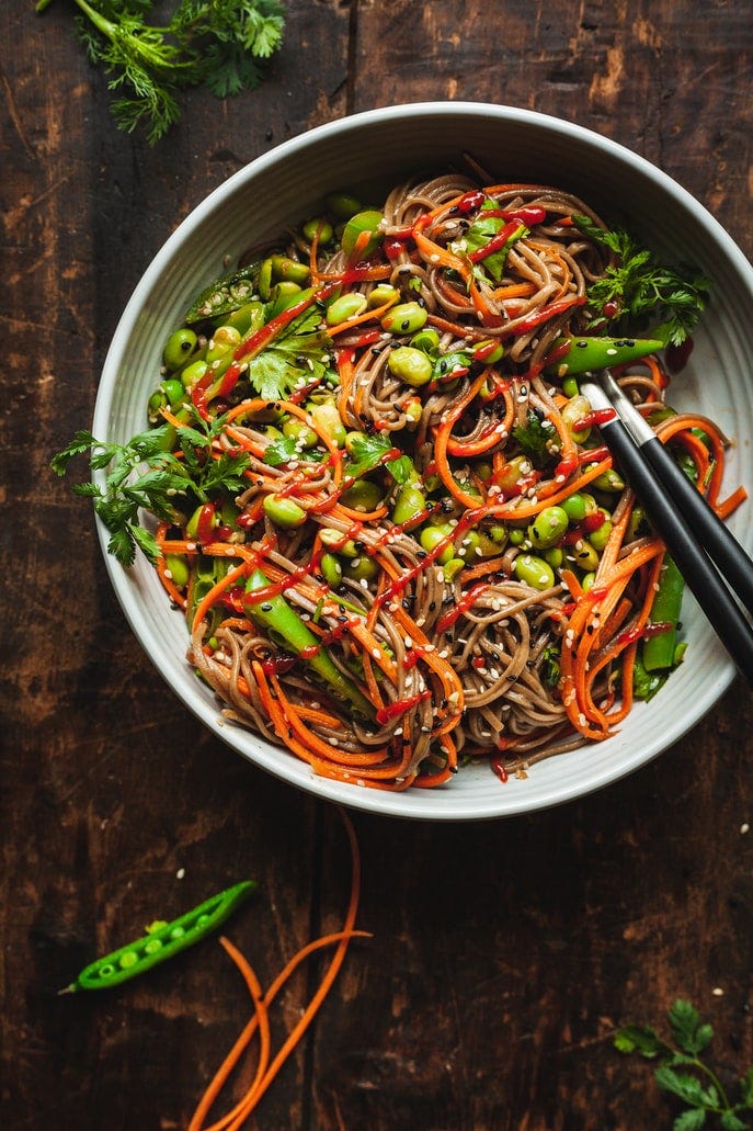 A bowl of soba noodles with broccoli, edamame, and carrots.