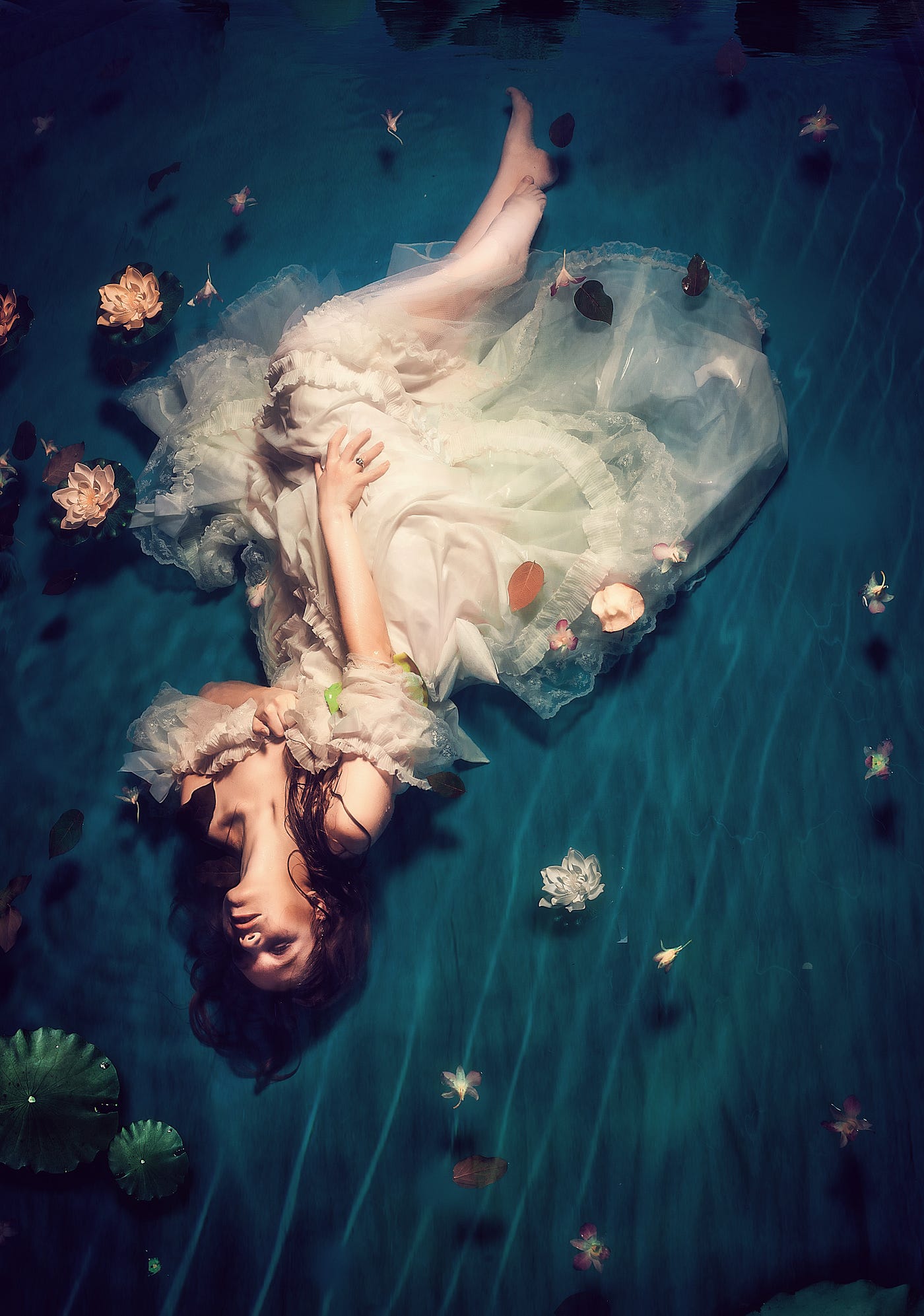 A woman in white dress under water, resting on the river bed, with intense emotions.