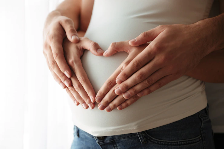 A woman and man making a heart with her hands on woman’s pregnant belly.