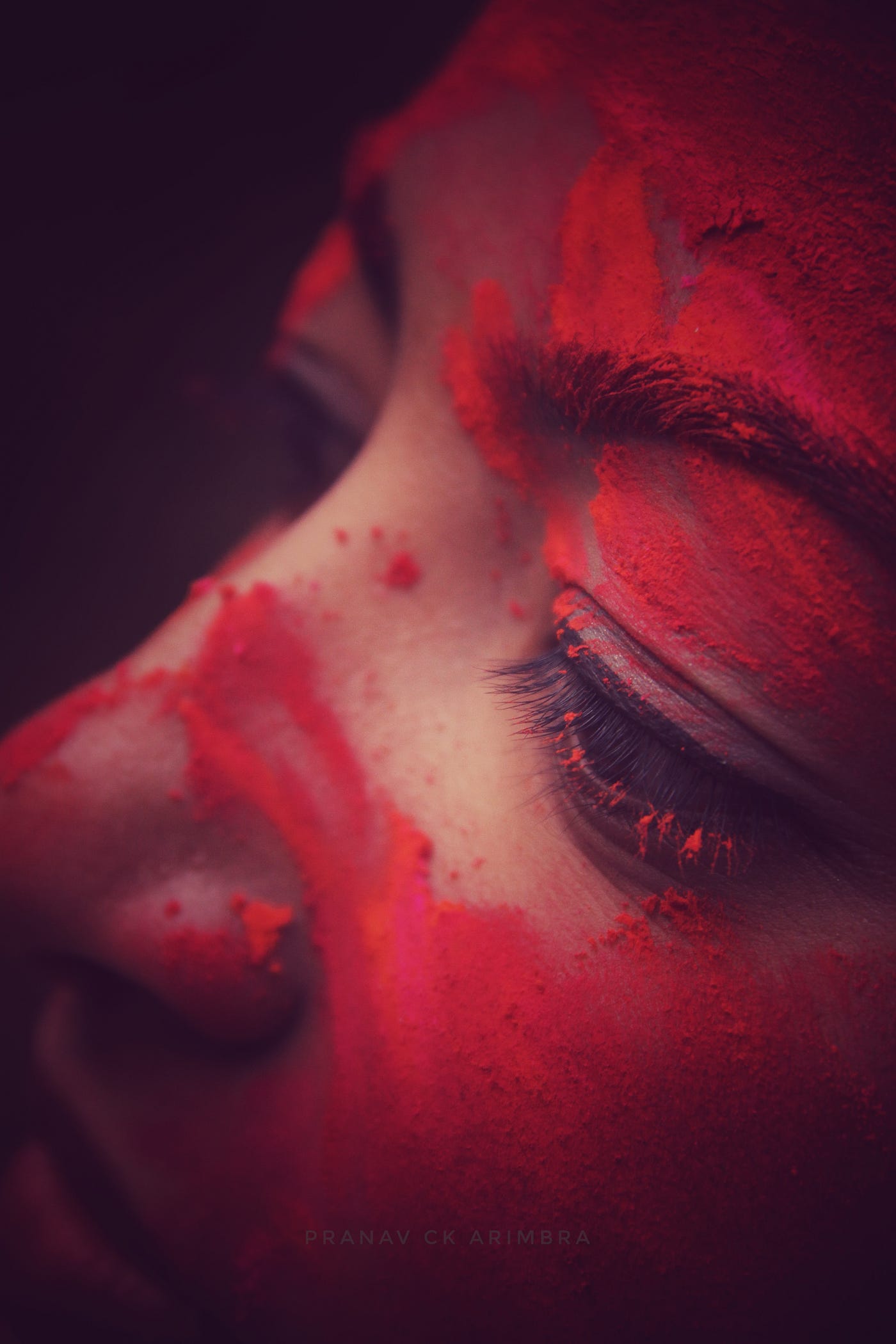 Woman with face in close-up, red paint splashed across her white face.