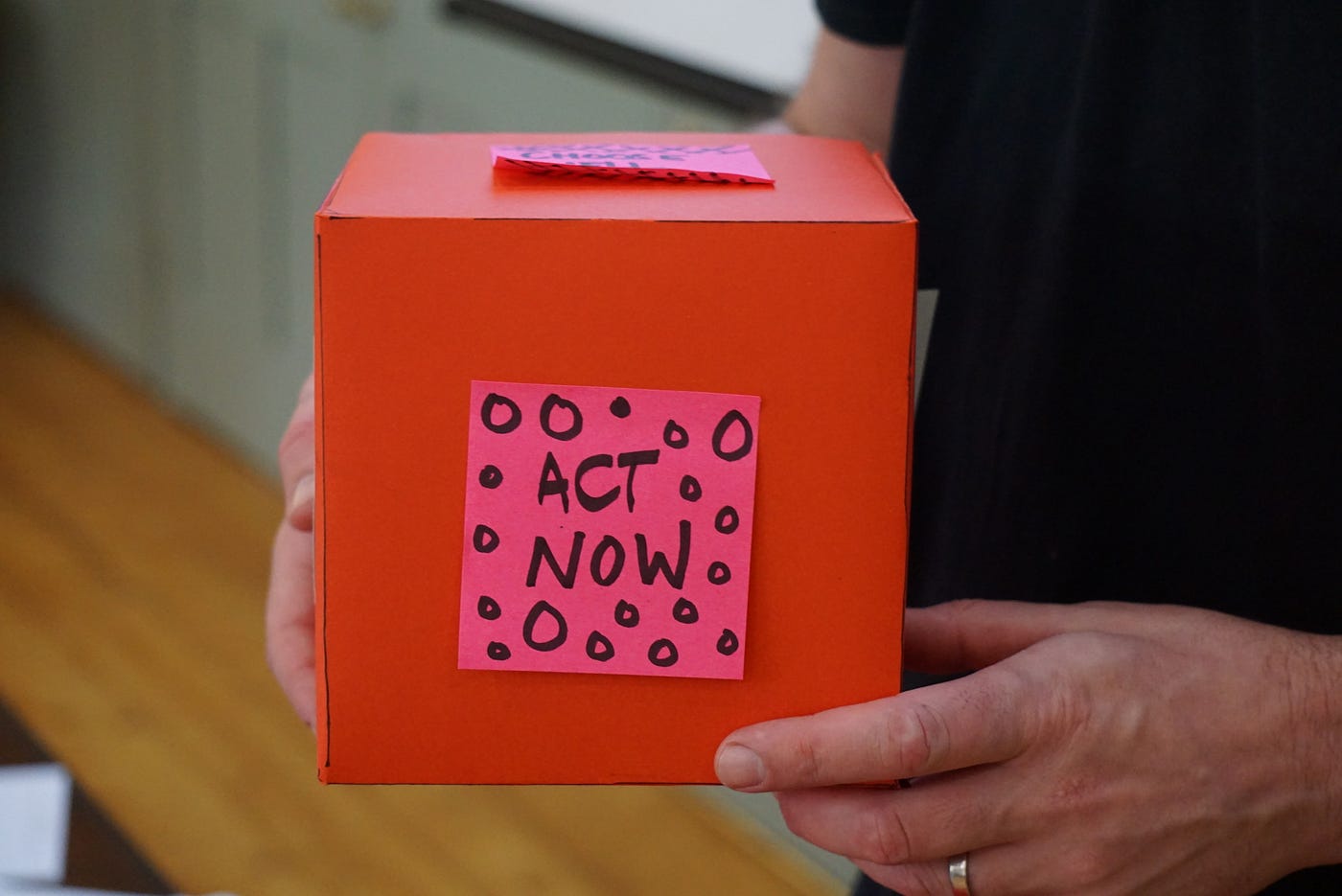 Person holding red box with “Act Now” sticky note
