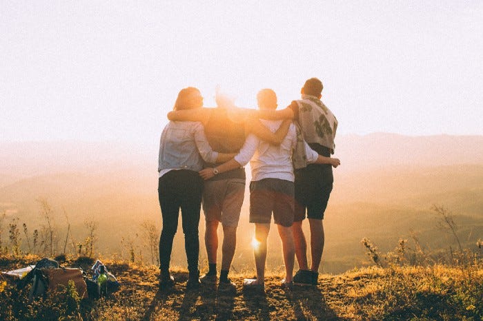 four people standing next to each other with arms on shoulders looking at the sunset