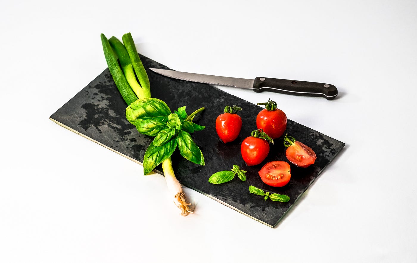 Cutting board (black), with 6 tomatoes and some vegetables. A knife sits on the edge of the small cutting board. New research suggests that a Mediterranean diet may help those with depression.