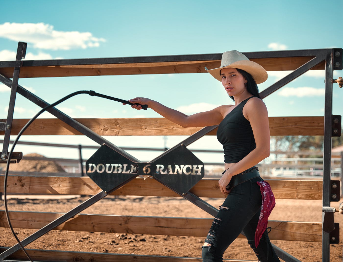 Girl wearing a cowboy hat, in a rodeo ring, brandishing a whip