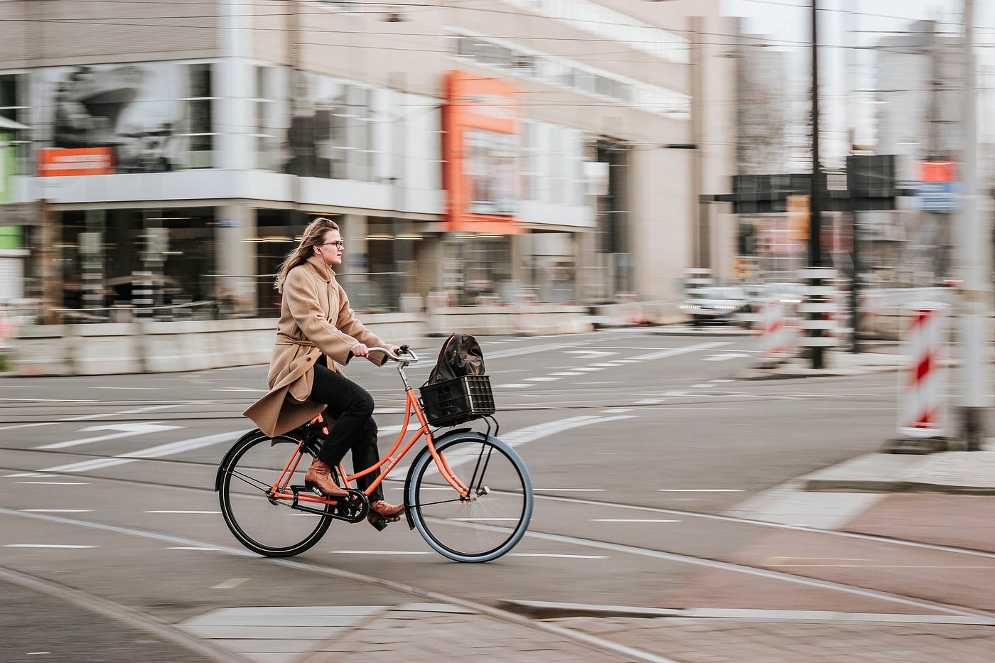 A woman rides an orange bike from left to right. Physical activity can reduce the risk of stroke.