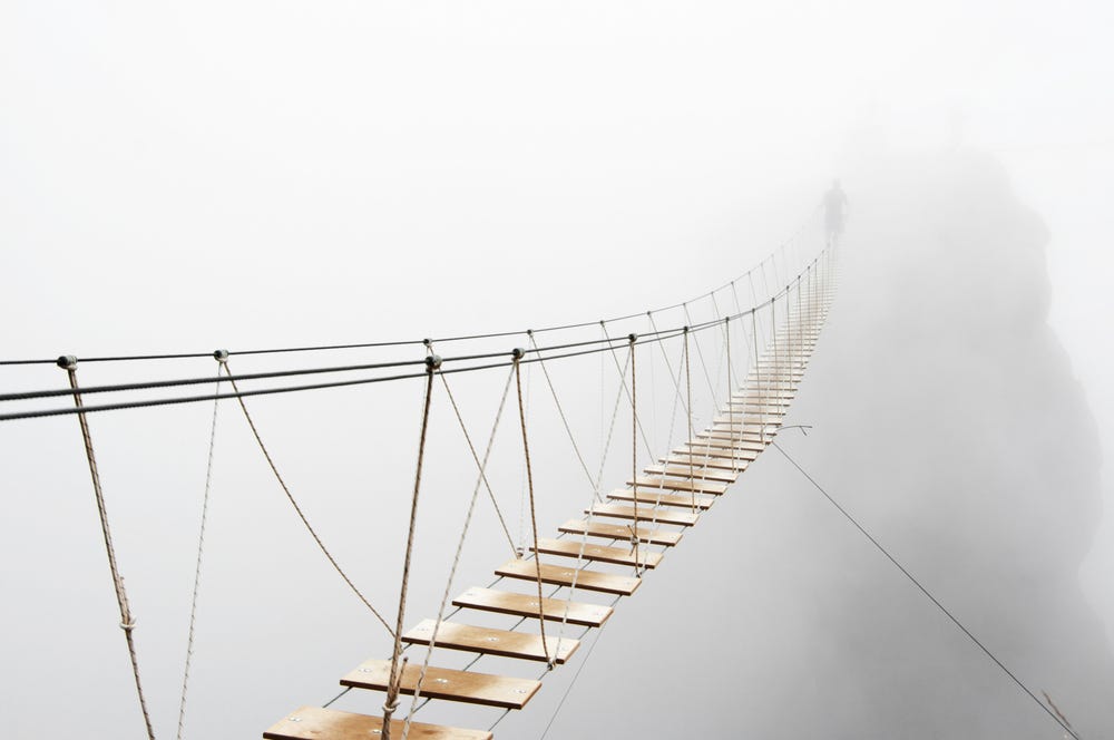 Man walking on hanging bridge vanishing in fog to indicate ambiguity