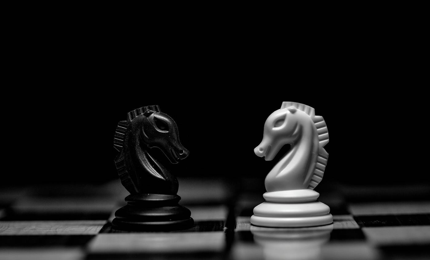 A black and white picture of a chessboard with one black knight and one white knight facing one another