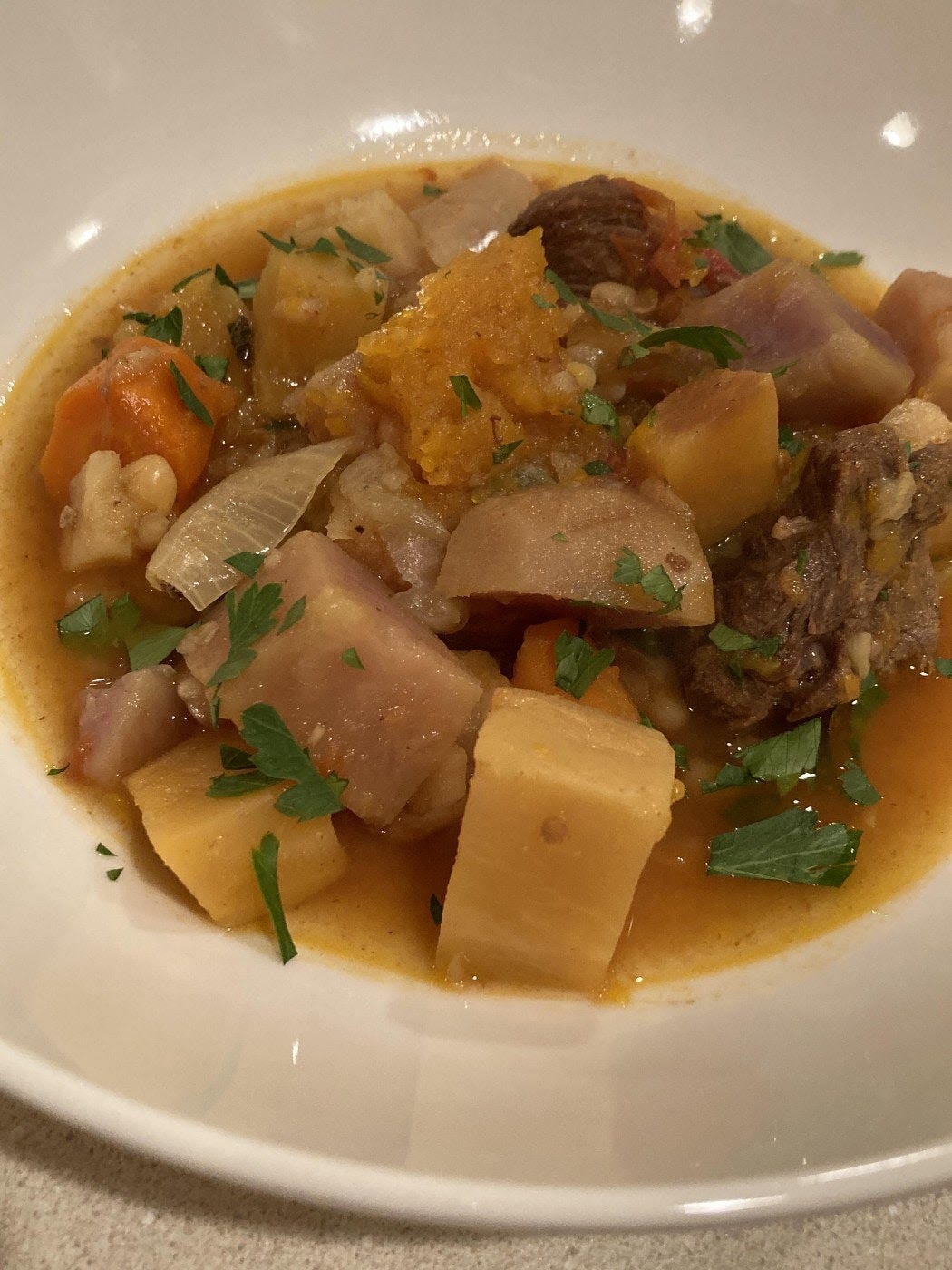 Shallow bowl of beef stew with large chunks of potato, garnished with chopped parsley.